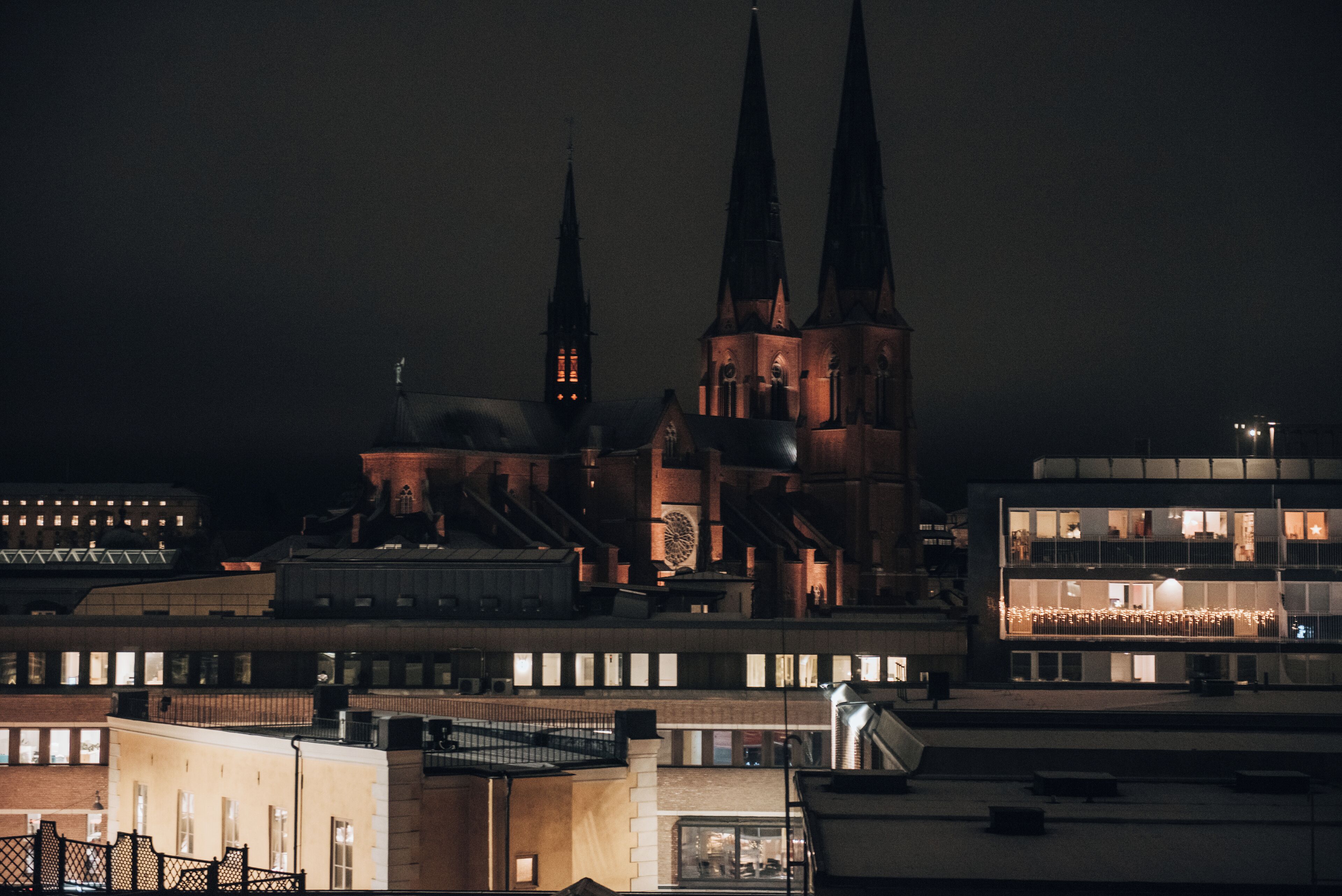 Vista nocturna de una iglesia con dos altas torres y un edificio moderno con ventanas iluminadas.
