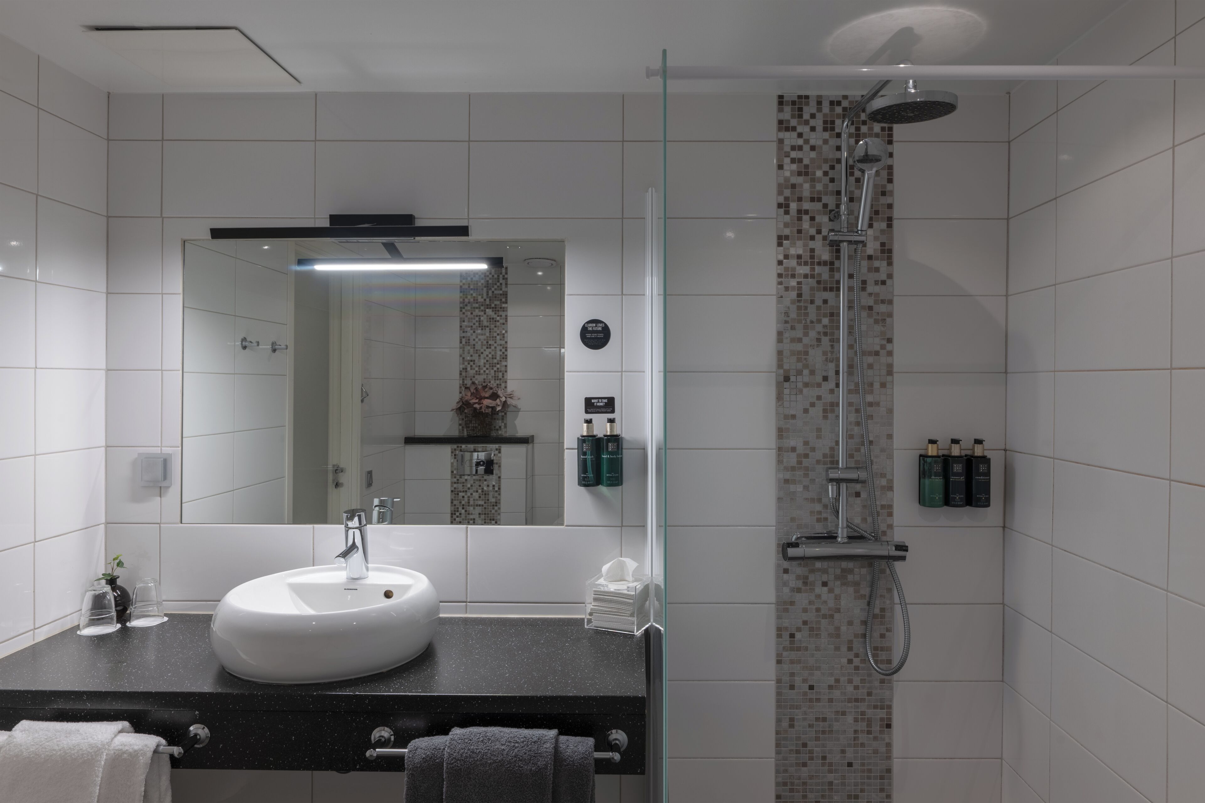 A modern bathroom with a white sink, a glass shower enclosure, and toiletries on the wall.