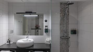 A modern bathroom with a white sink, a glass shower enclosure, and toiletries on the wall.