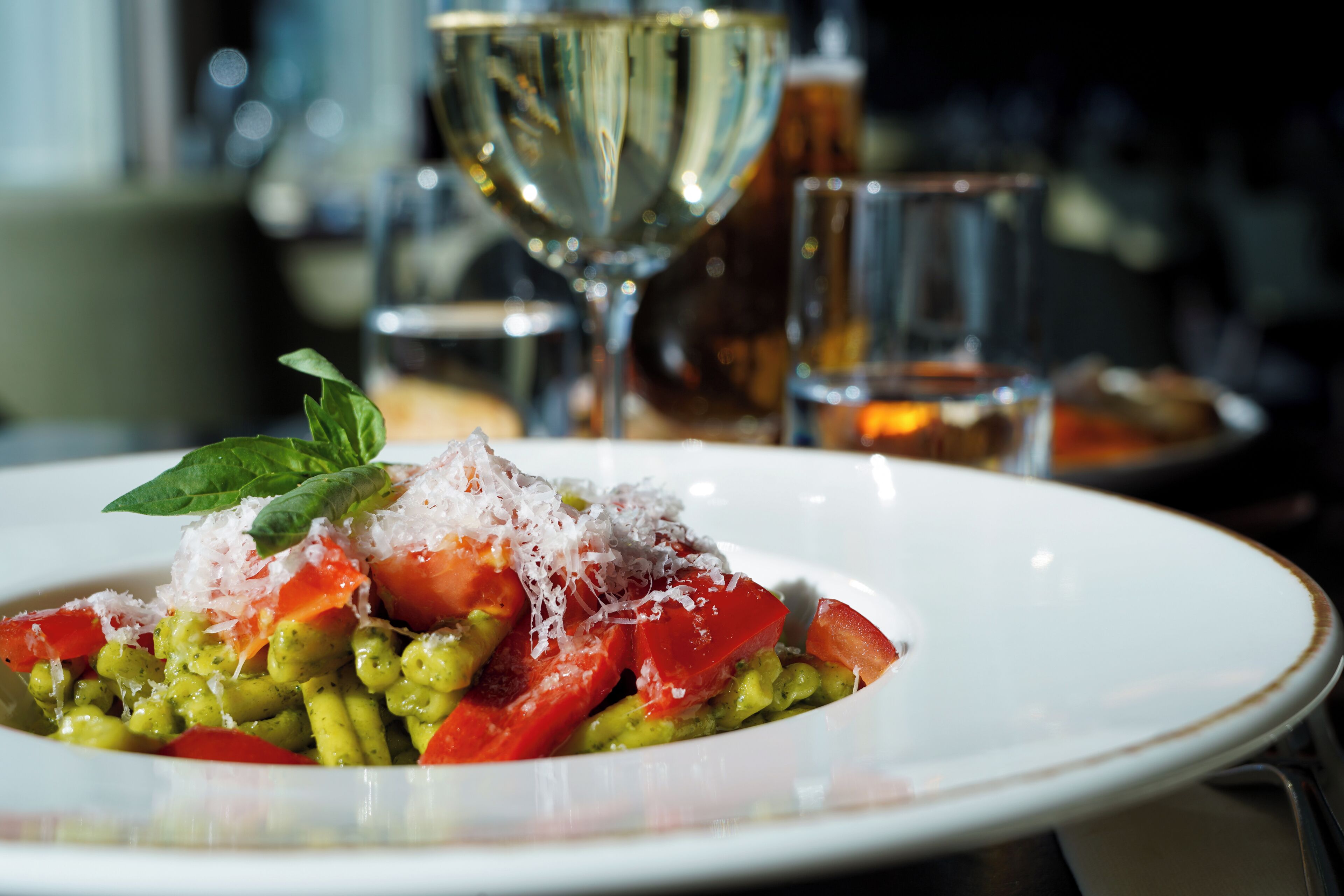 A plate of pasta with tomatoes and cheese, a glass of wine, and a glass of water on a table.