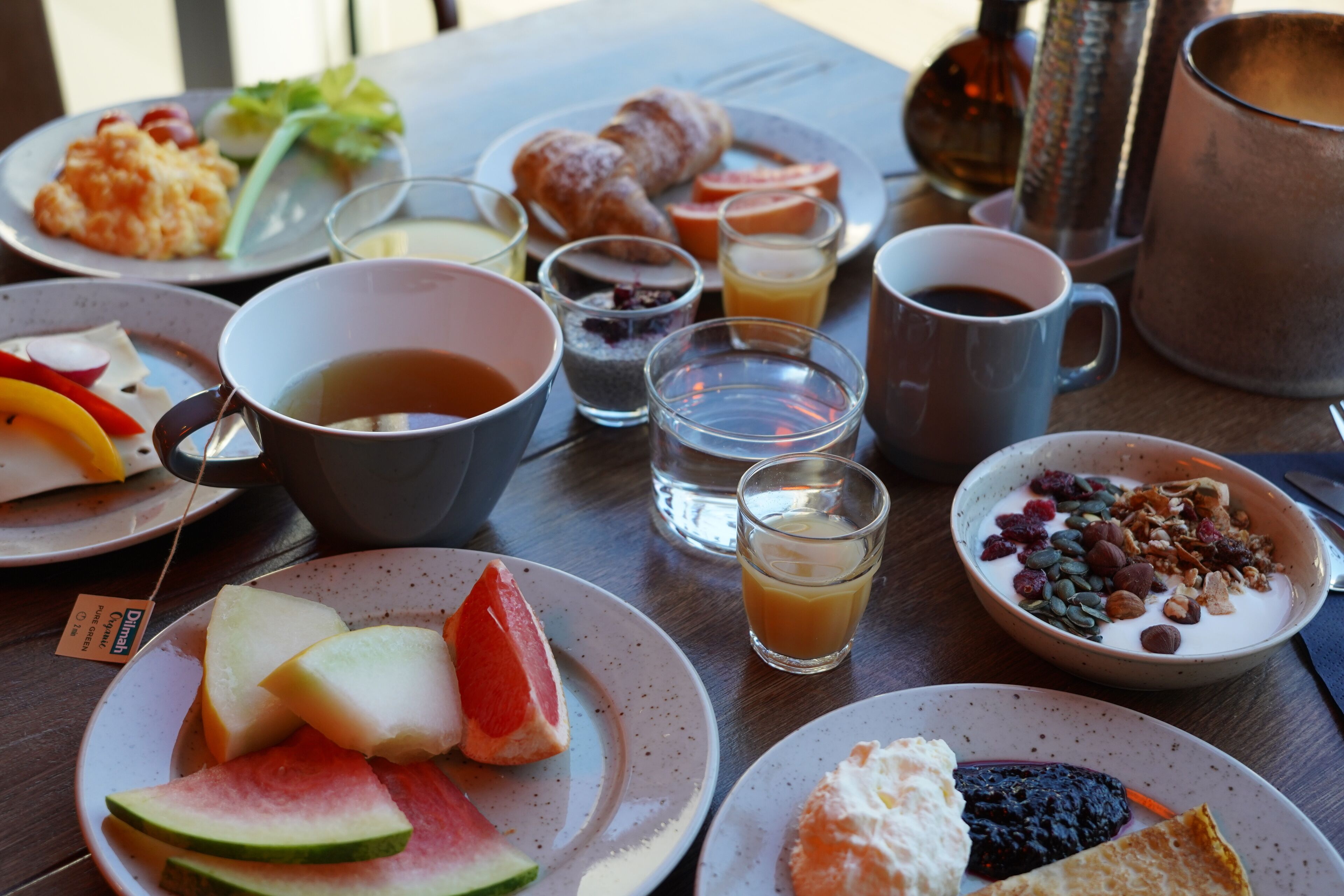 Una mesa de desayuno con platos de comida, tazas y una tetera.