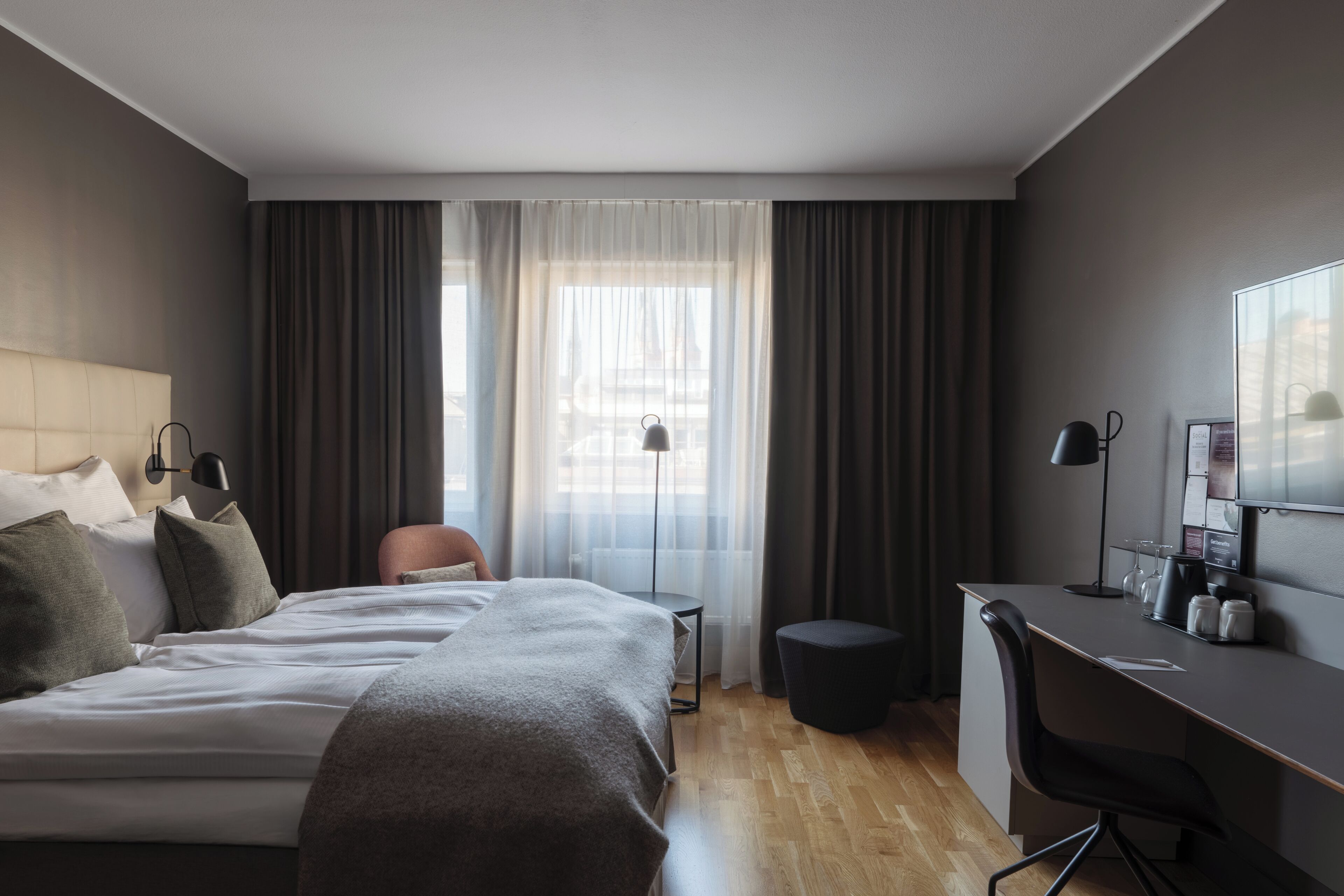Una habitación de hotel moderna con una cama grande, un escritorio, una silla y un taburete pequeño.