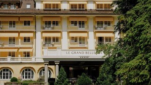 Un hotel de varios pisos con una visible bandera suiza, una entrada principal y un jardín bien cuidado con una fuente.