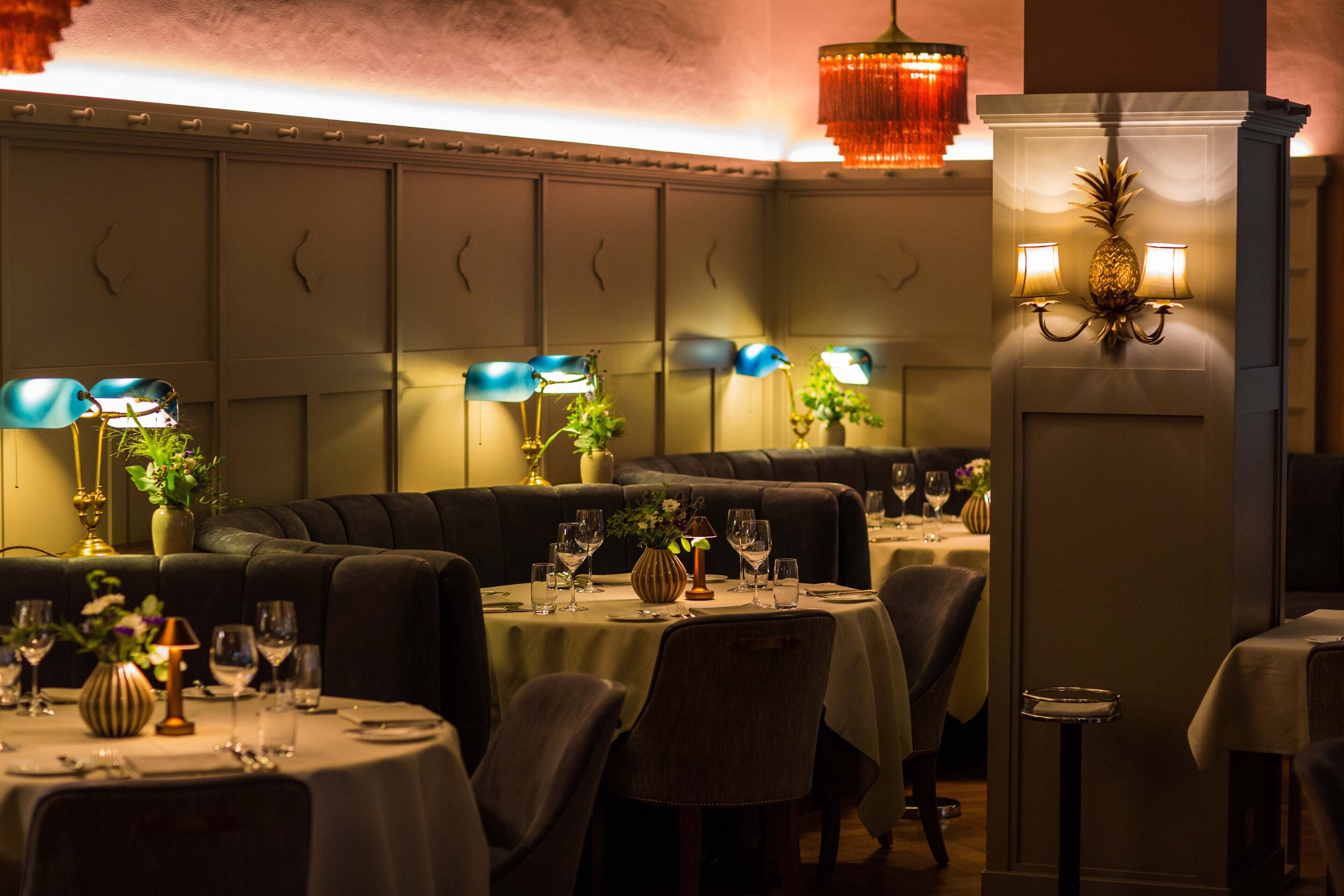 Ein Restaurant mit Sitzboxen und runden Tischen, an denen Weingläser und Besteck bereitstehen.