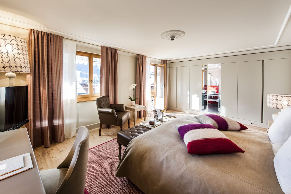 Habitación de hotel con cama, escritorio, silla, televisor y ventana con cortinas.