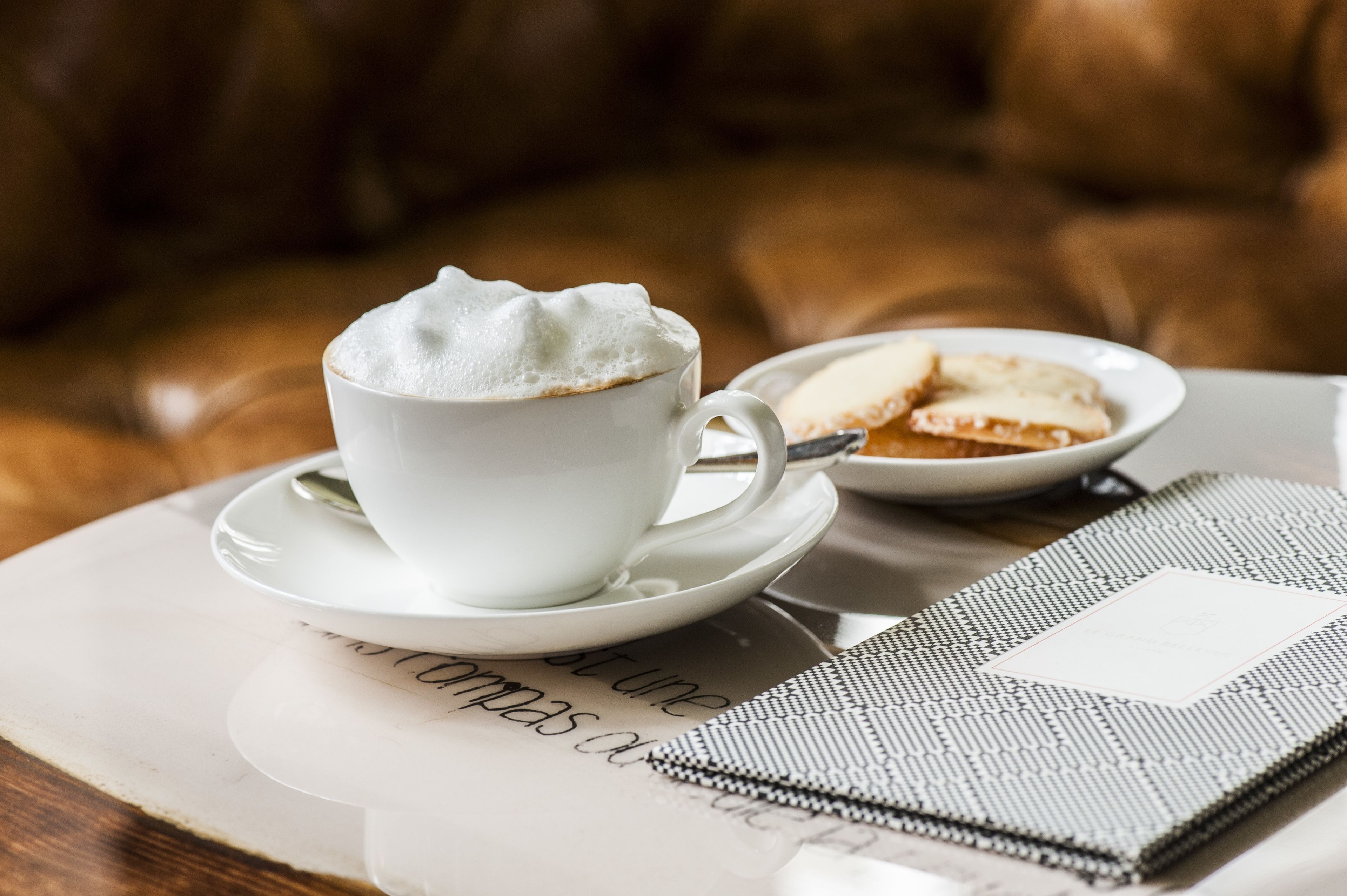 Une tasse de café blanc, posée sur une soucoupe, avec une assiette de biscuits à proximité.
