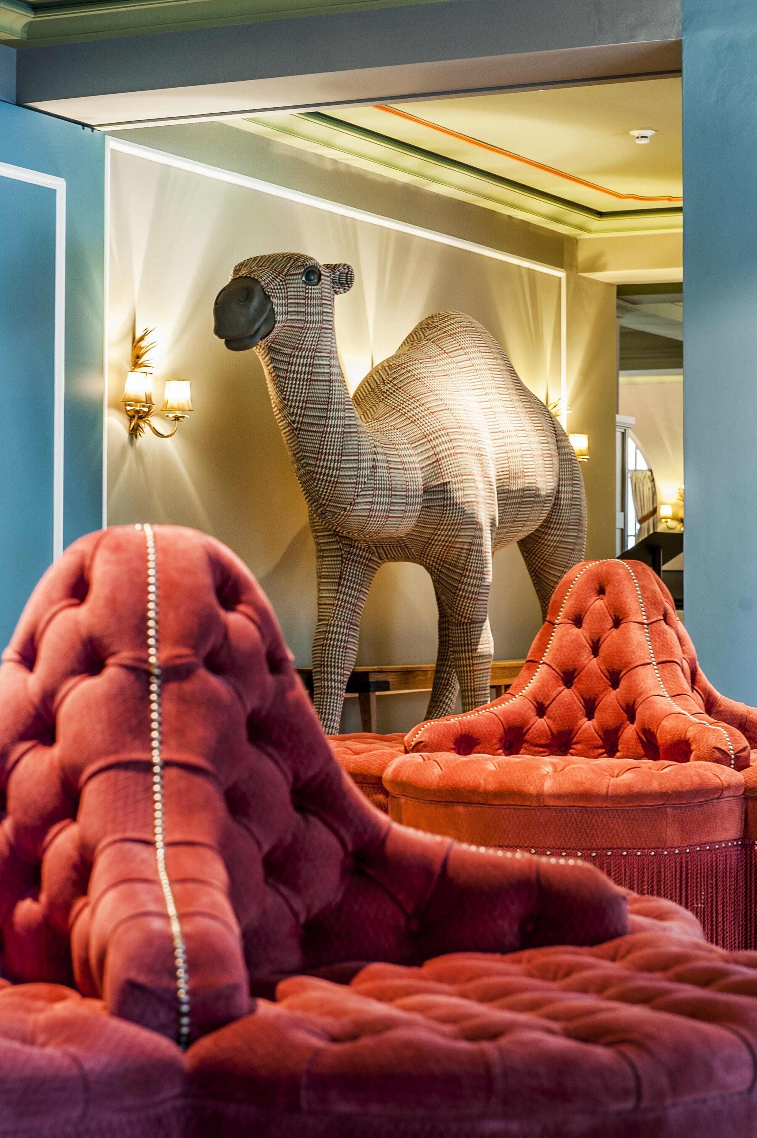 Een kamer met een grote kameelbeeld, een rode sofa met pluizen en een wandlamp.
