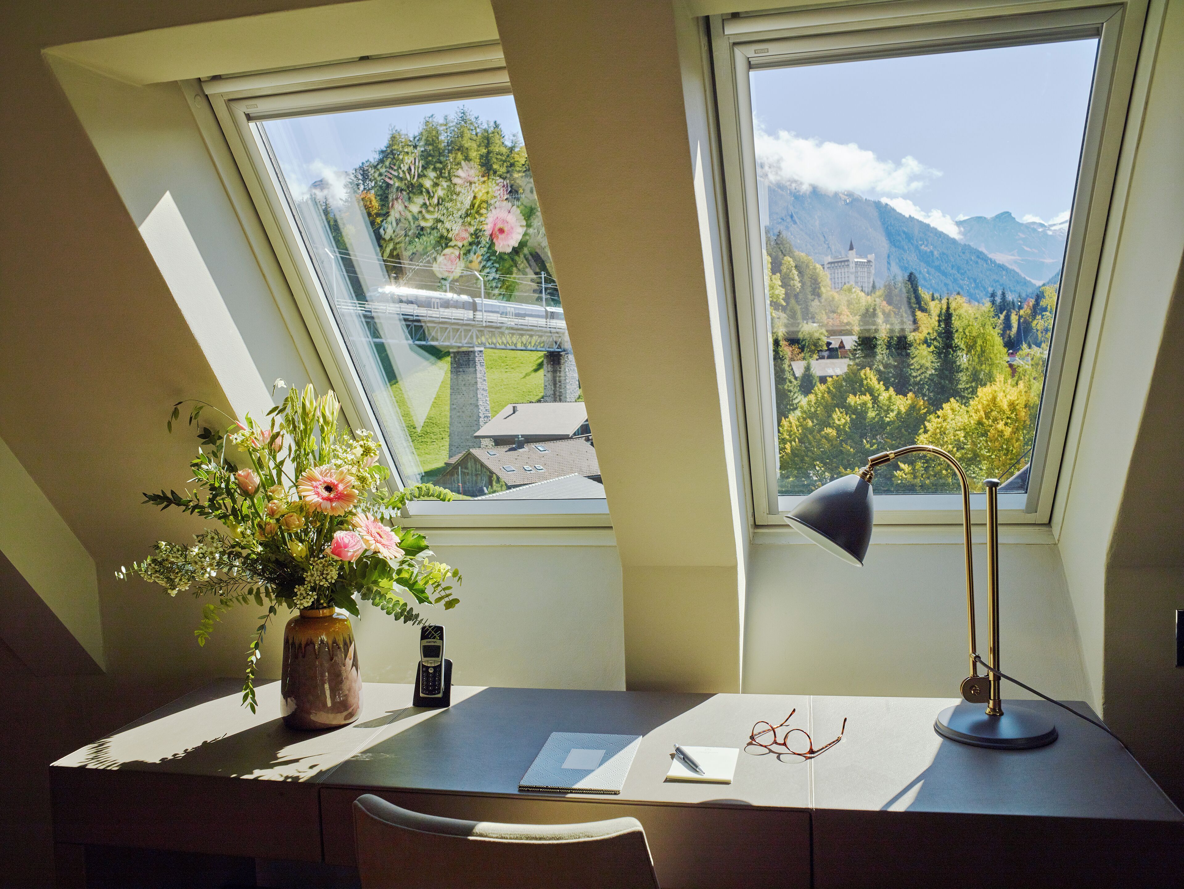 A desk with a vase of flowers, a lamp, and a pair of glasses.