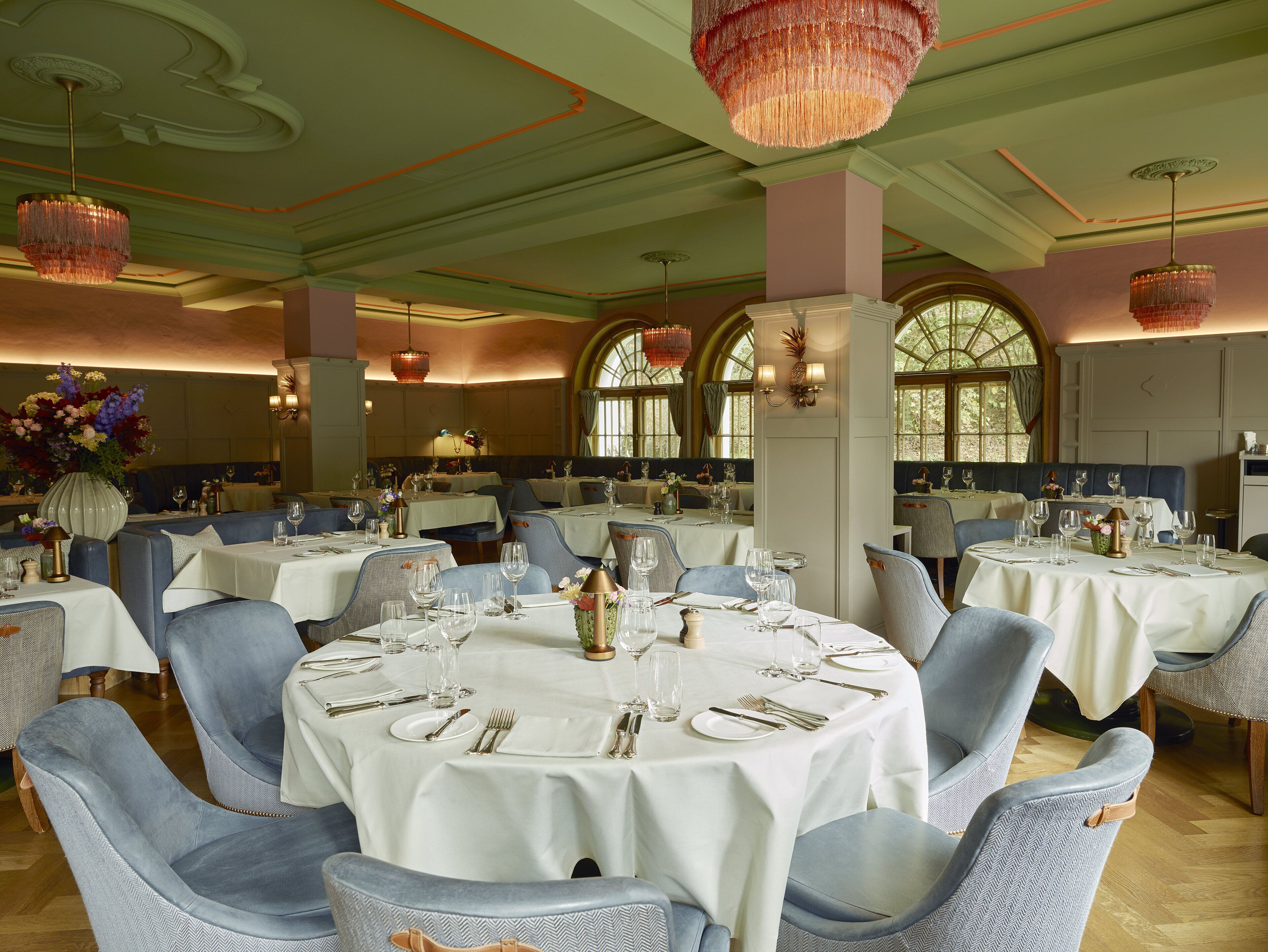 A formal dining room with round tables, blue upholstered chairs, and ornate chandeliers.