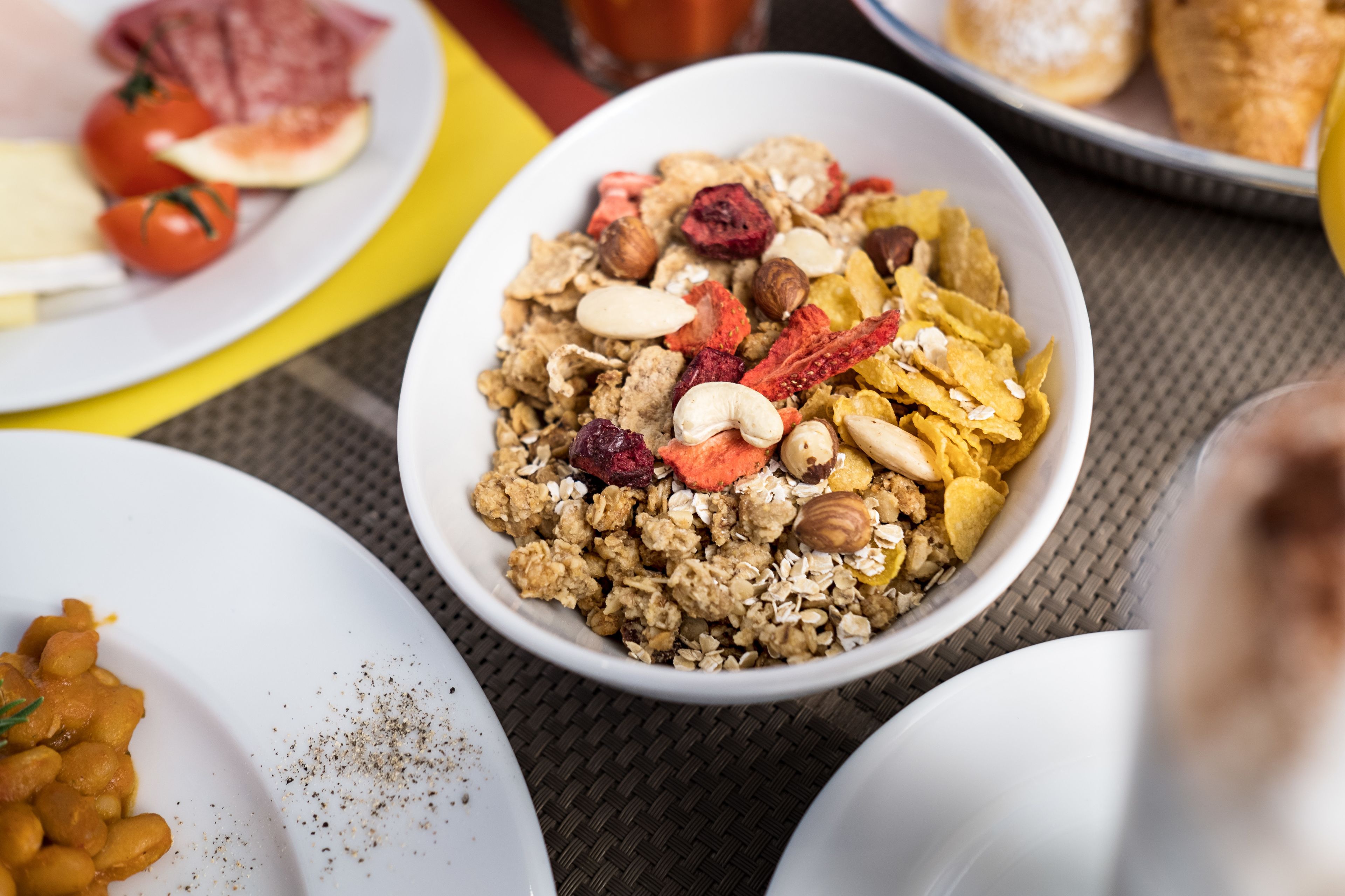 A breakfast setting with various dishes including cereal, fruits, and nuts.