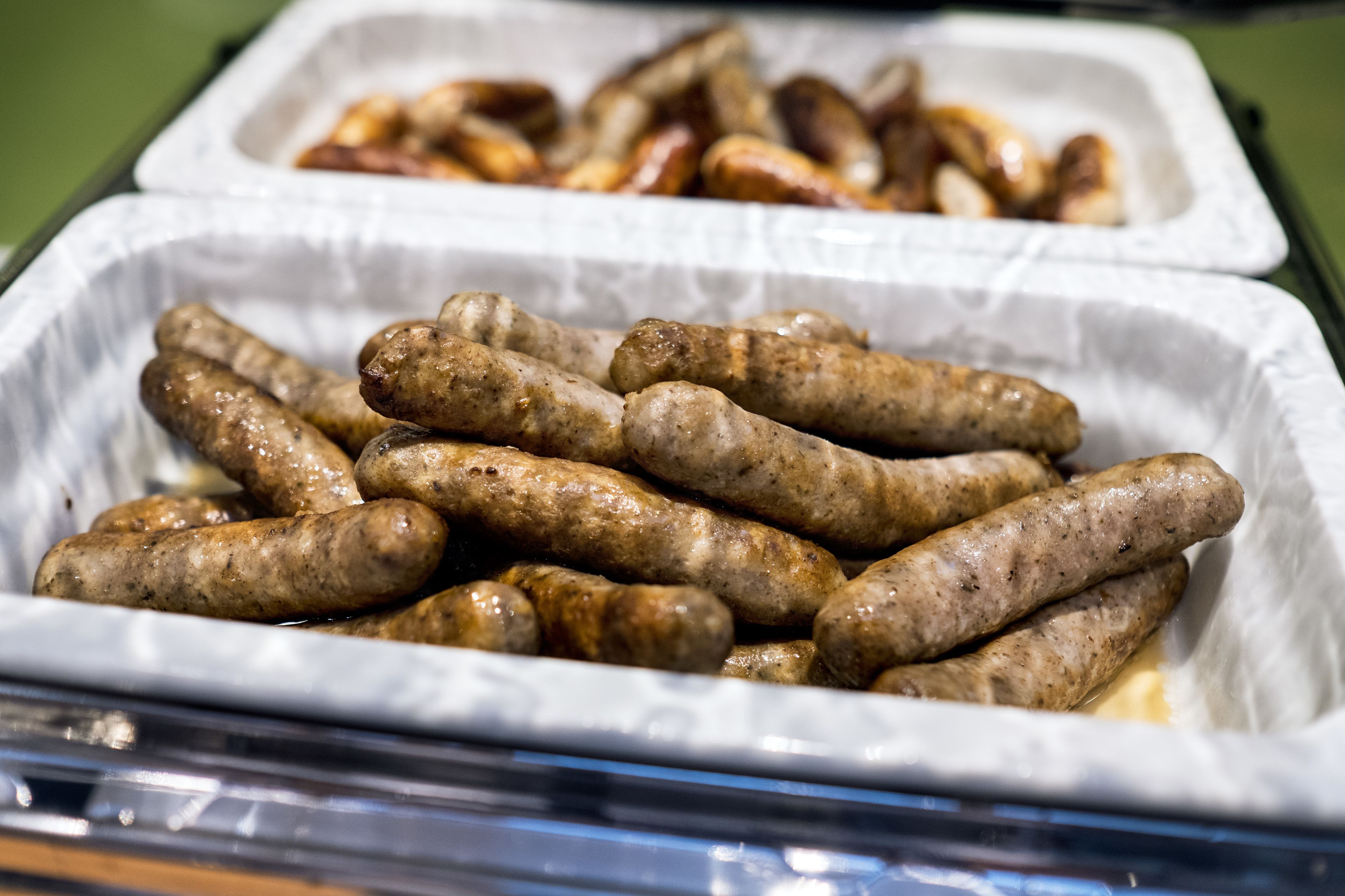 A tray of cooked sausages in a white paper container.