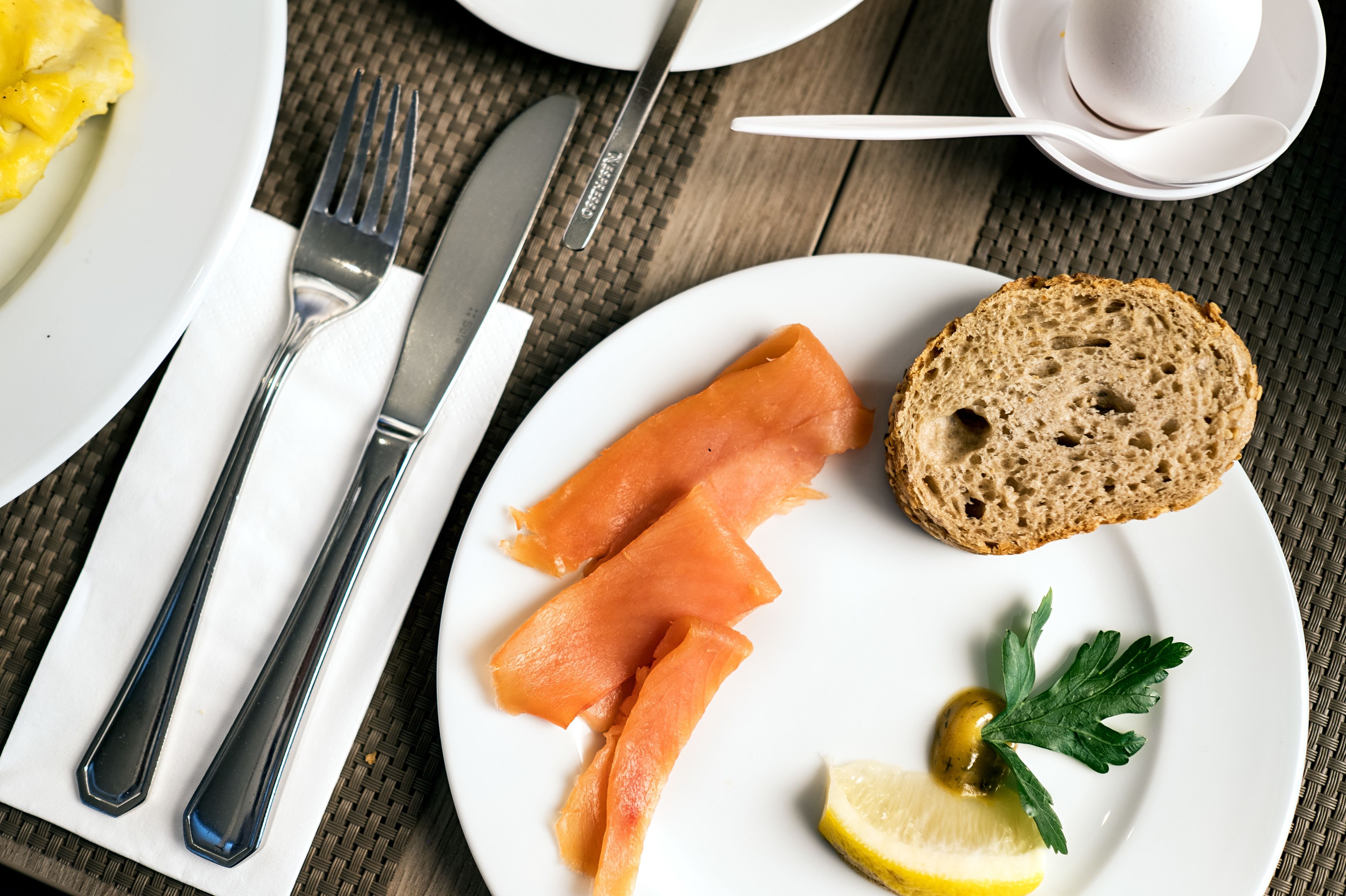 A plate with smoked salmon, a slice of bread, a lemon wedge, and a sprig of parsley.