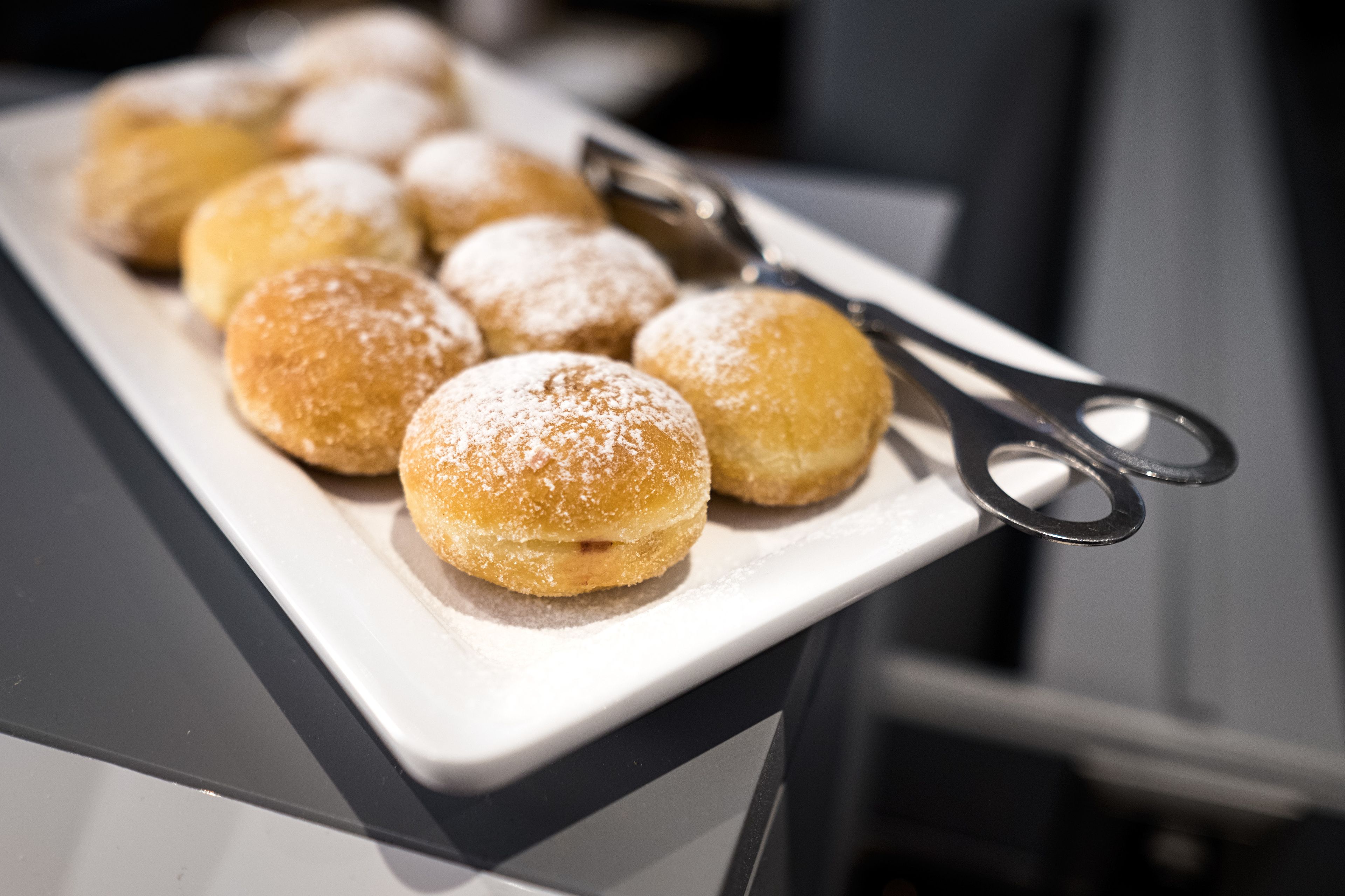 A white rectangular plate with several round pastries dusted with powdered sugar, placed on a dark surface.
