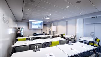 Une salle de conférence avec des tables et des chaises blanches, ainsi qu’un écran de projection.