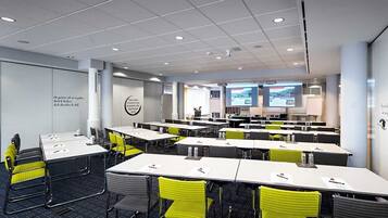A conference room with multiple tables and chairs, equipped with presentation screens and a projector.