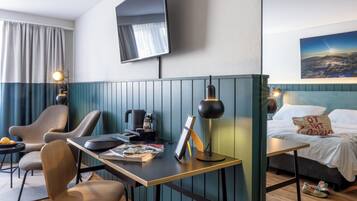 Ein Hotelzimmer mit Schreibtisch, Stühlen, einem Bett, einem Fernseher und einem Bild an der Wand.