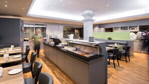 Un restaurante moderno con un bufé central, zonas de estar y una cocina al fondo.