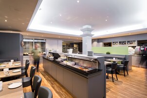 Un restaurante moderno con un bufé central, zonas de estar y una cocina al fondo.
