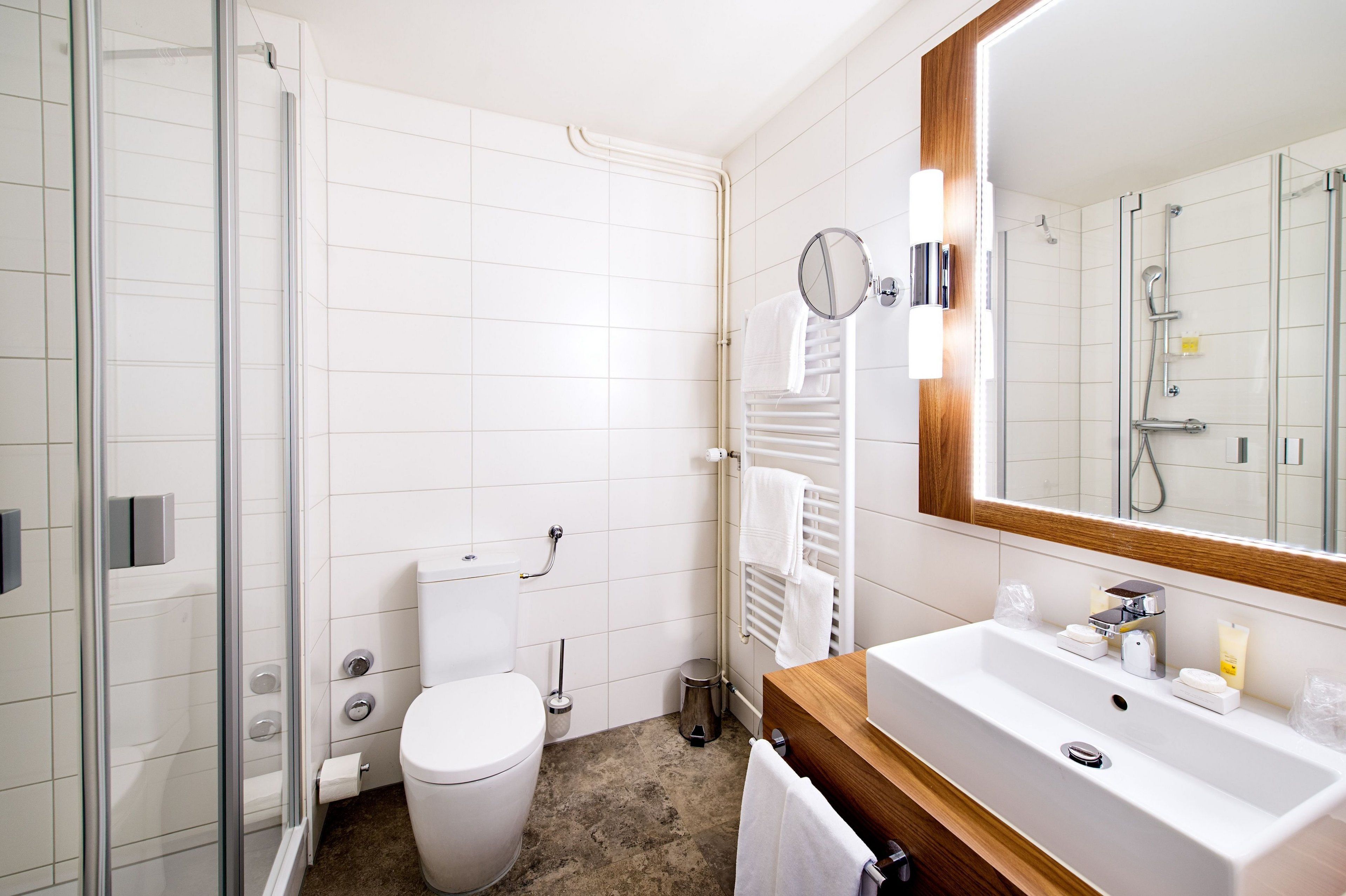 Un baño moderno con cabina de ducha de vidrio, inodoro blanco, lavamanos con tocador de madera y espejo con marco de madera.