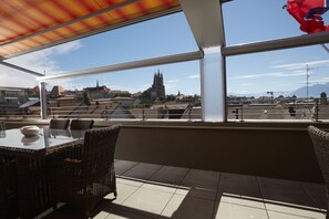 An outdoor dining area with wicker furniture and a view of a church and mountains in the background. - Hotel Crystal (Lausanne)