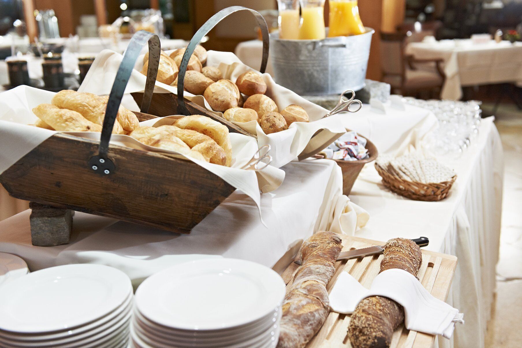 Una mesa de buffet con panes y pastelería variados, incluyendo cruasanes y baguettes, y una cesta de mimbre para pan.
