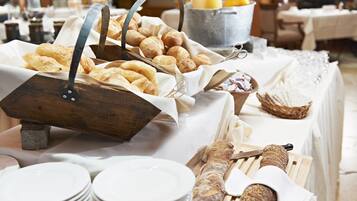 Una mesa de buffet con panes y pastelería variados, incluyendo cruasanes y baguettes, y una cesta de mimbre para pan.