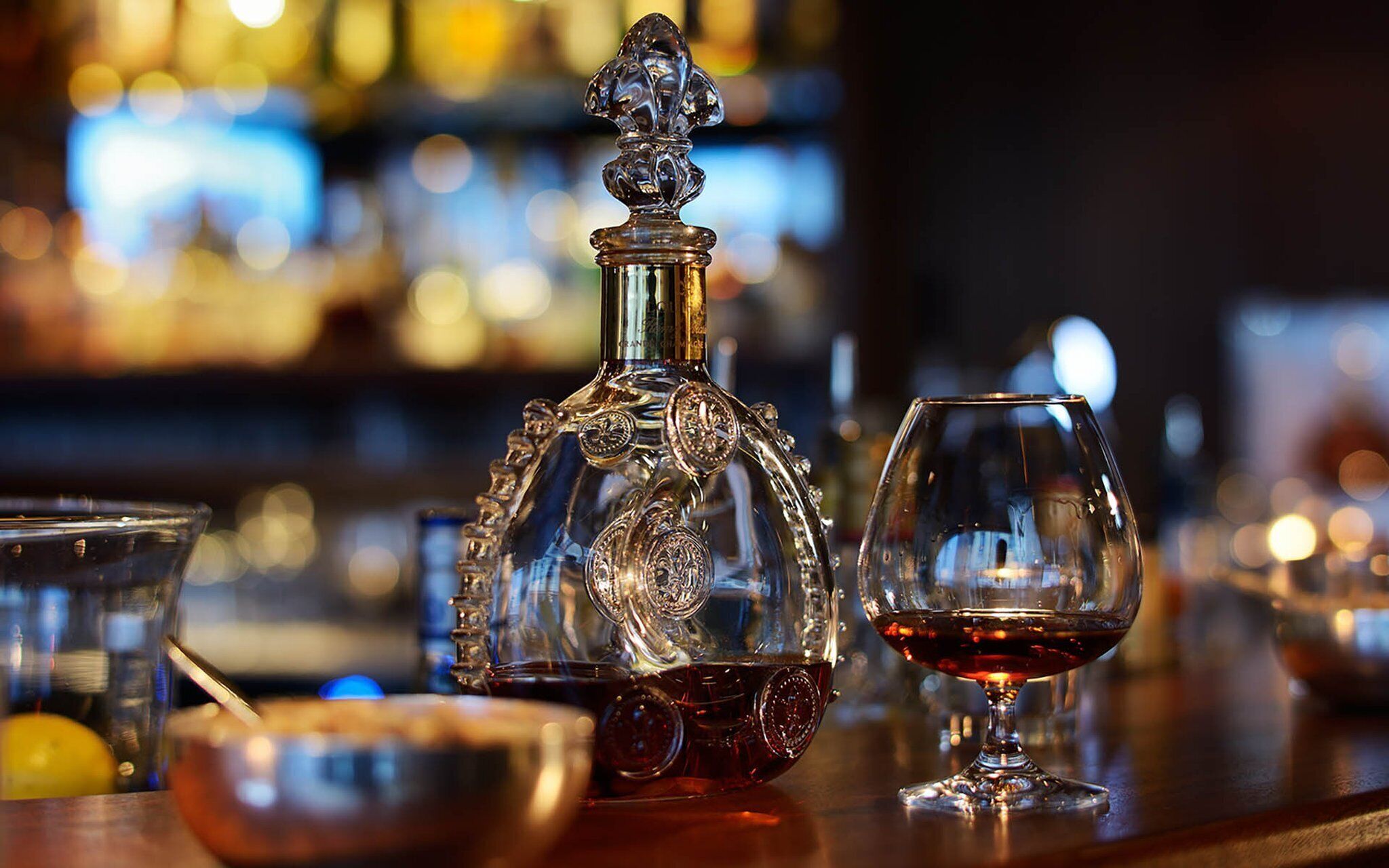 A bar setting with a decanter, a glass of red wine, and a bowl of lemons.