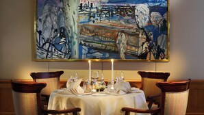 A dining table set with white tablecloth, candles, and wine glasses, surrounded by upholstered chairs with a striped pattern. - Crystal Hotel (St. Moritz)