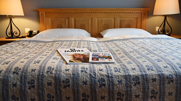 A bed with a floral-patterned bedspread, two pillows, and two magazines titled 'St. Matz' and 'Top Tips'.