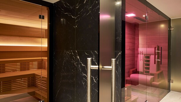 A modern spa room with a wooden bench, a glass partition, and a massage table. - Crystal Hotel (St. Moritz)