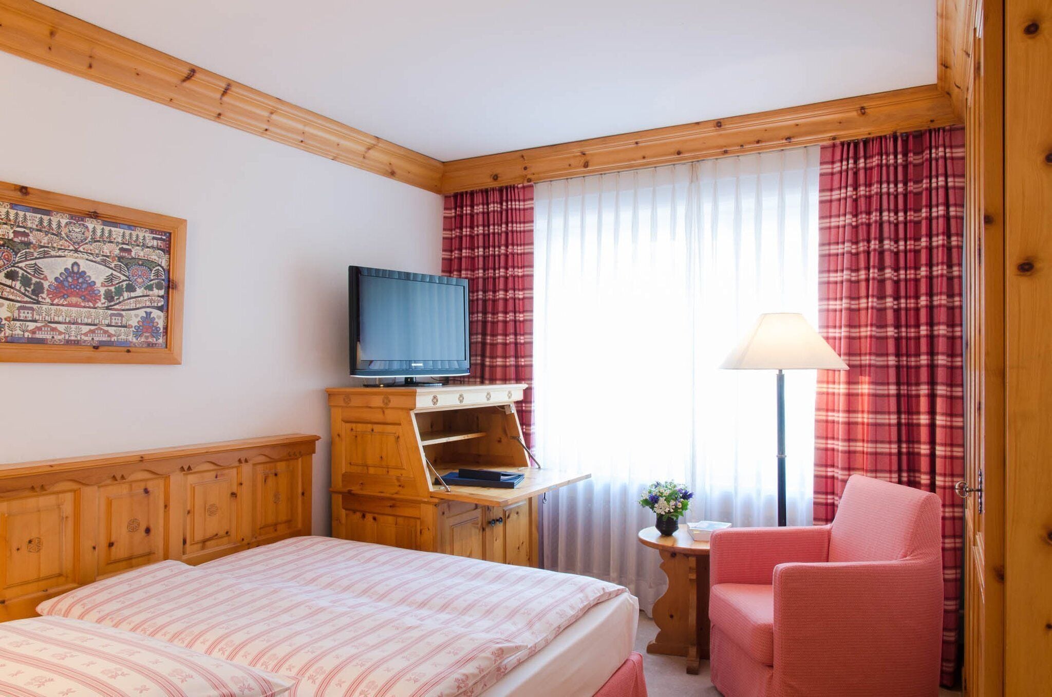 A hotel room with a bed, a television on a wooden cabinet, a small table with a lamp, and a chair.