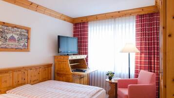 A hotel room with a bed, a television on a wooden cabinet, a small table with a lamp, and a chair.