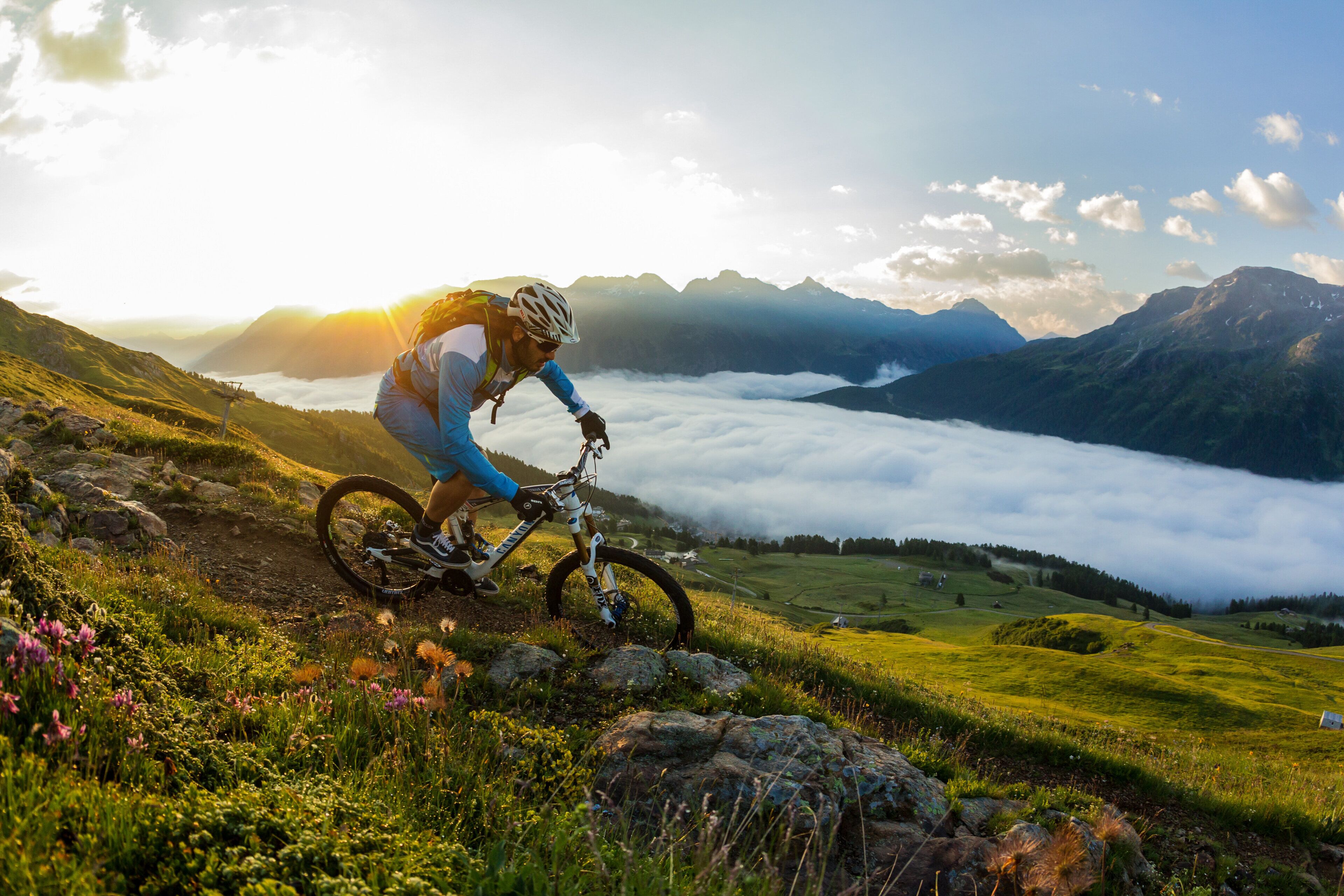 A mountain biker on a trail with a view of a valley and mountains in the background.