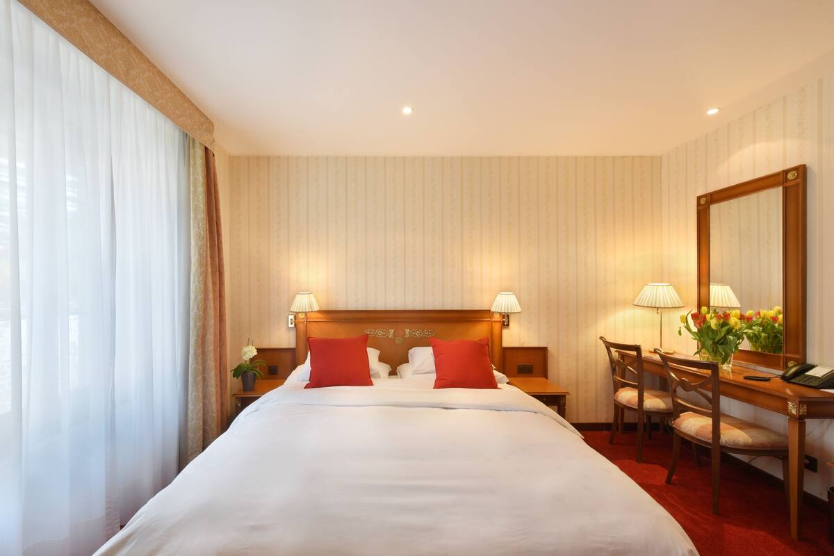 A hotel room with a large bed, two bedside lamps, a desk with a chair, and a mirror.