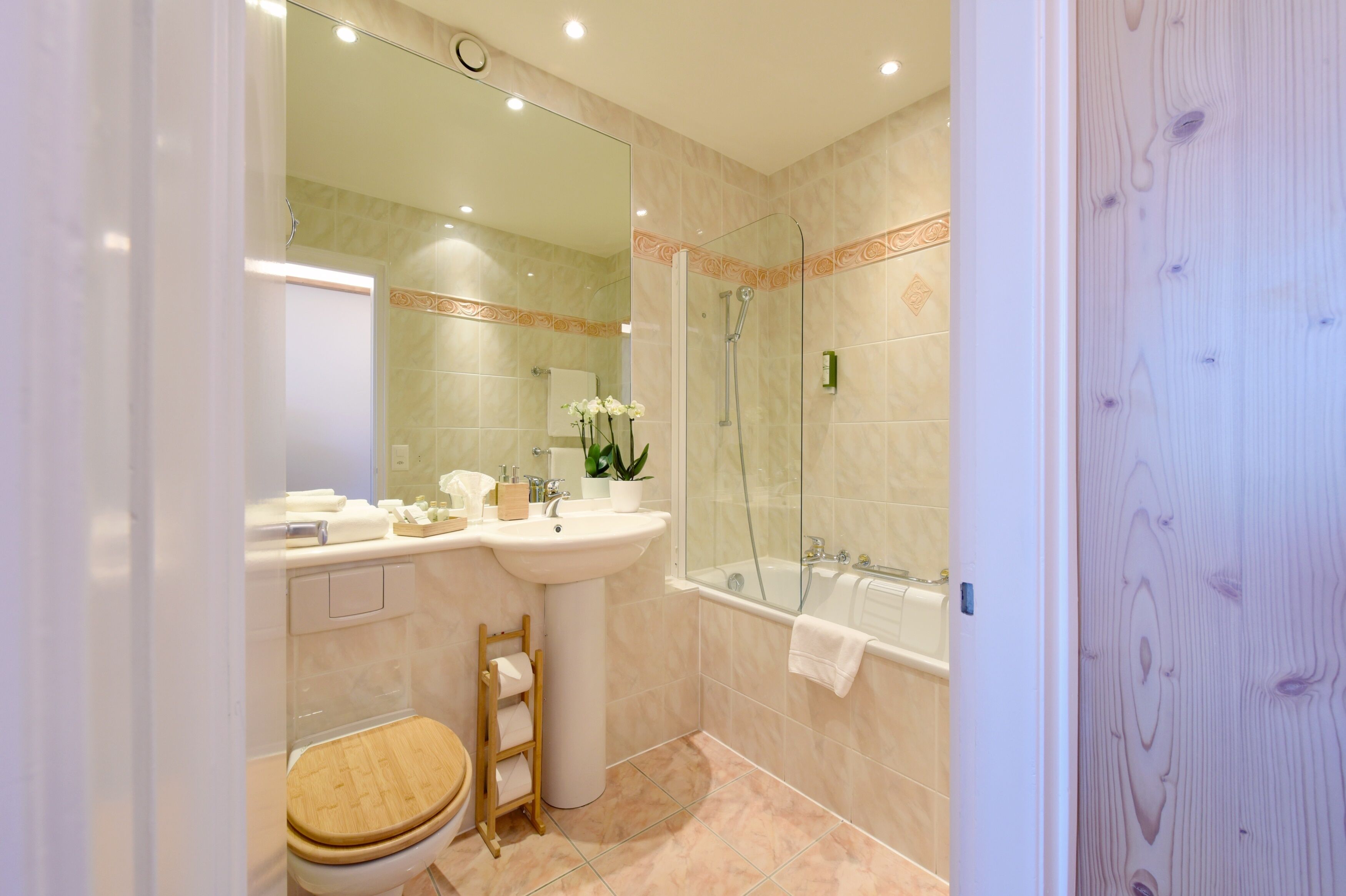 A bathroom with a toilet, sink, mirror, shower, and a wooden chair.