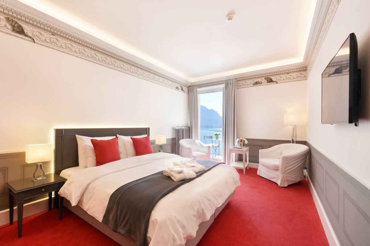 A hotel room with a large bed, a desk, a chair, a TV, and a view of the sea.