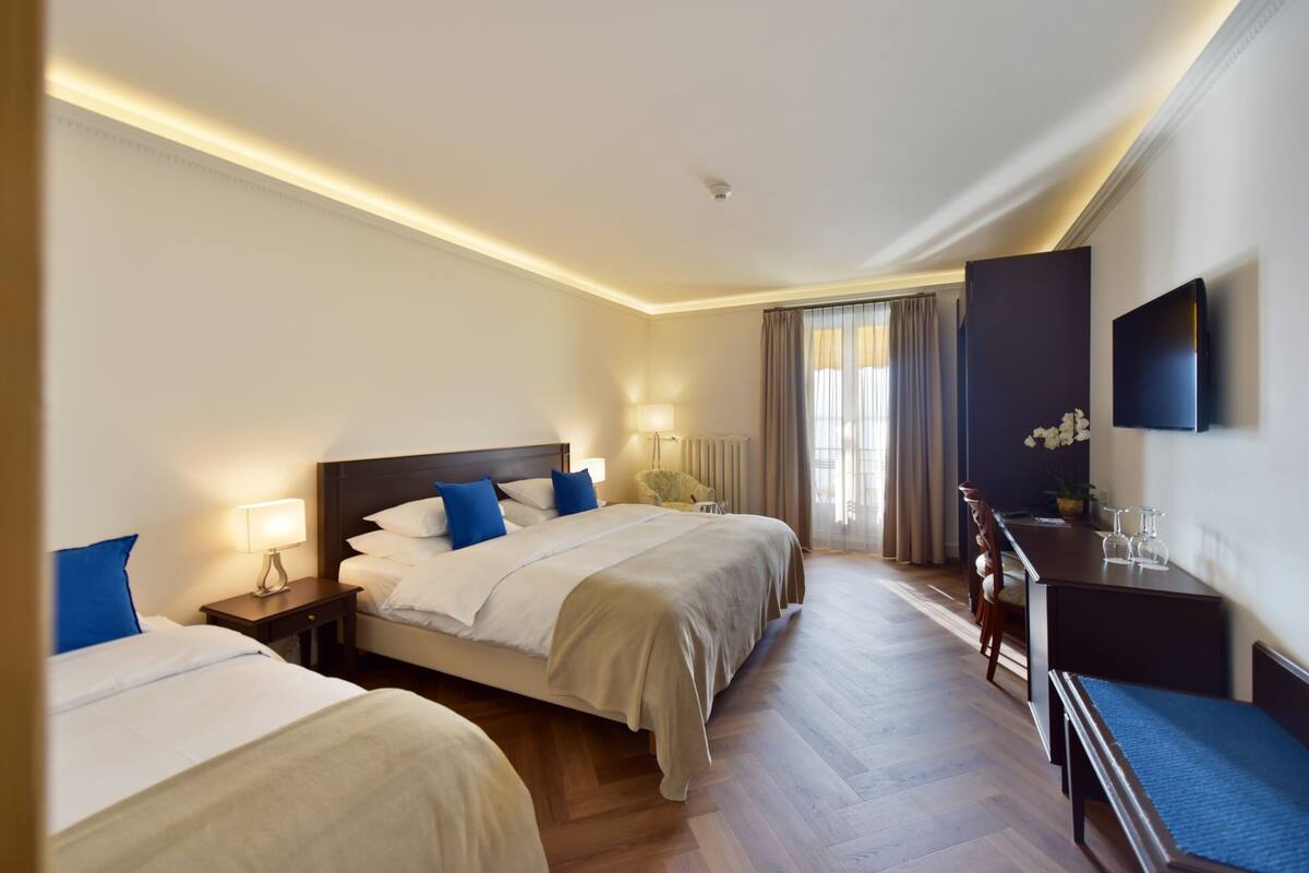 A hotel room with two beds, a desk, a chair, and a television.