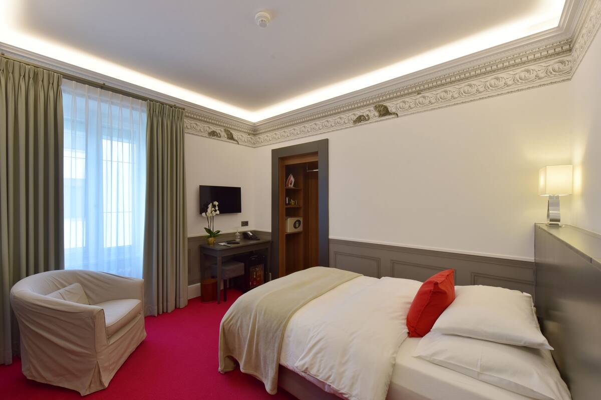 A hotel room with a bed, a desk, a chair, and a wardrobe.