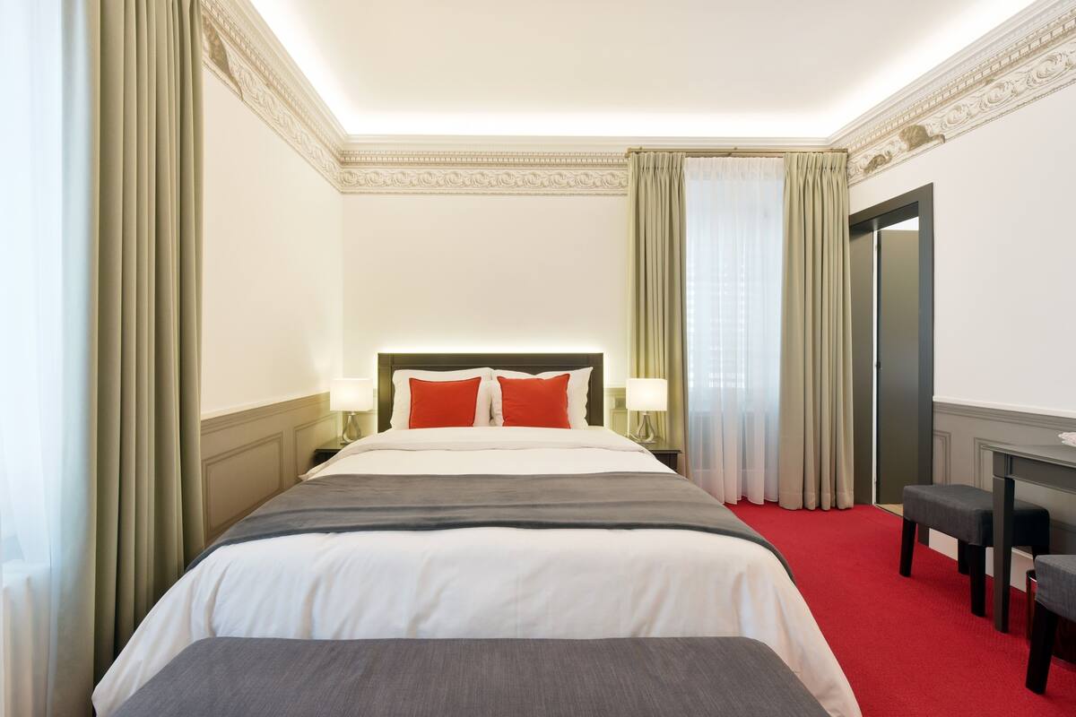 A hotel room with a large bed, two bedside tables with lamps, a desk, and a chair.