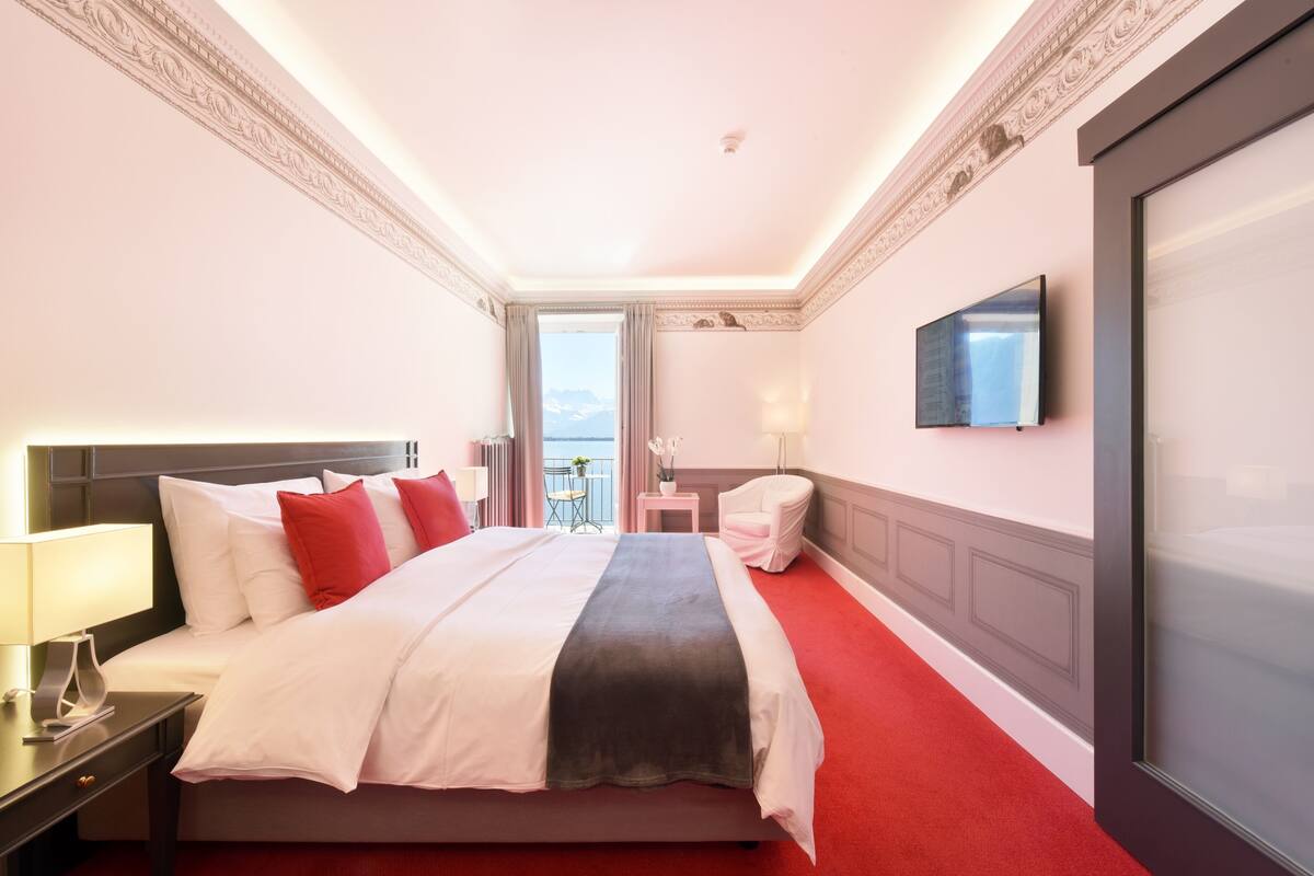 A hotel room with a large bed, a TV, a chair, and a balcony with a view.