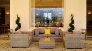 Un rincón exterior acogedor con mobiliario de mimbre y un amplio ventanal con vistas a un comedor.