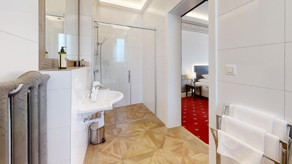 A modern bathroom with a glass shower enclosure, a white sink, and a red carpeted floor.