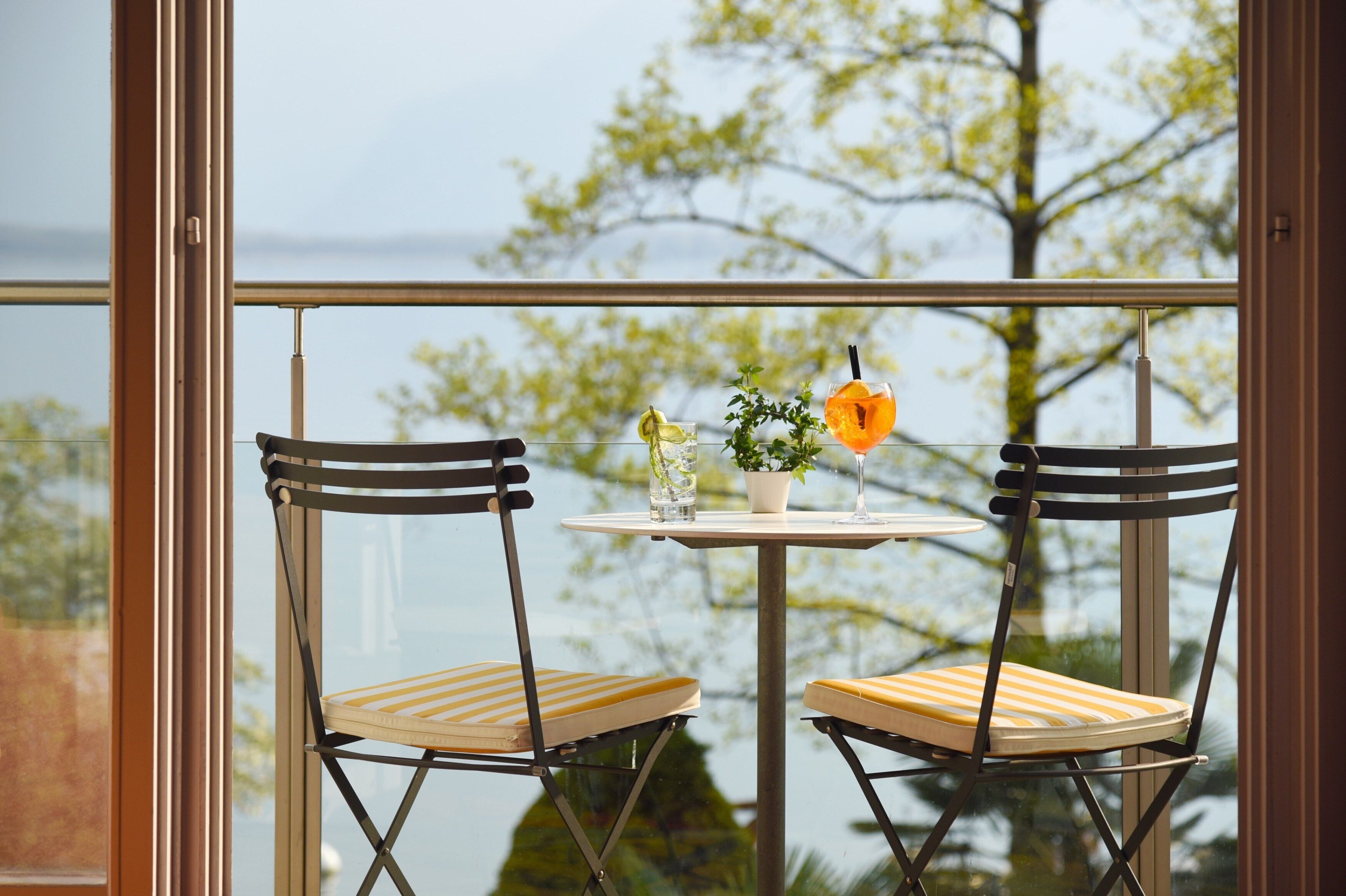 A balcony with two chairs and a small table, a potted plant, and a glass with a straw.