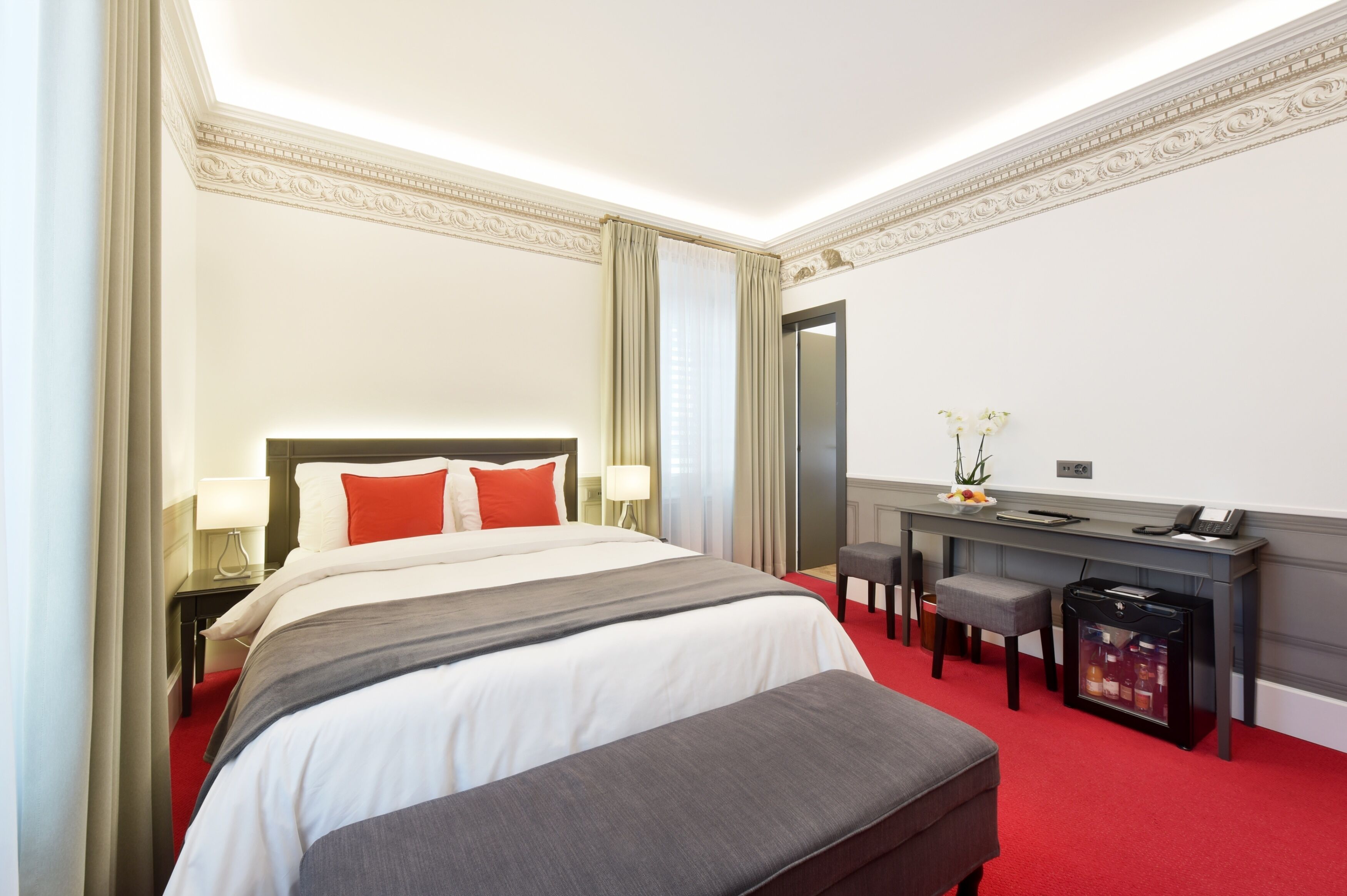 A hotel room with a large bed, a desk, a chair, and a minibar.