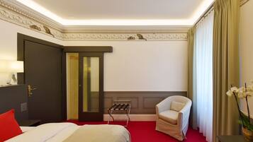 A hotel room with a bed, a chair, a desk, and a window with curtains.