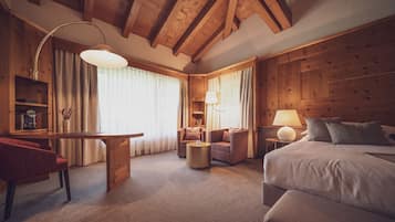 A cozy hotel room with a wooden ceiling, a bed, a desk, and two armchairs.