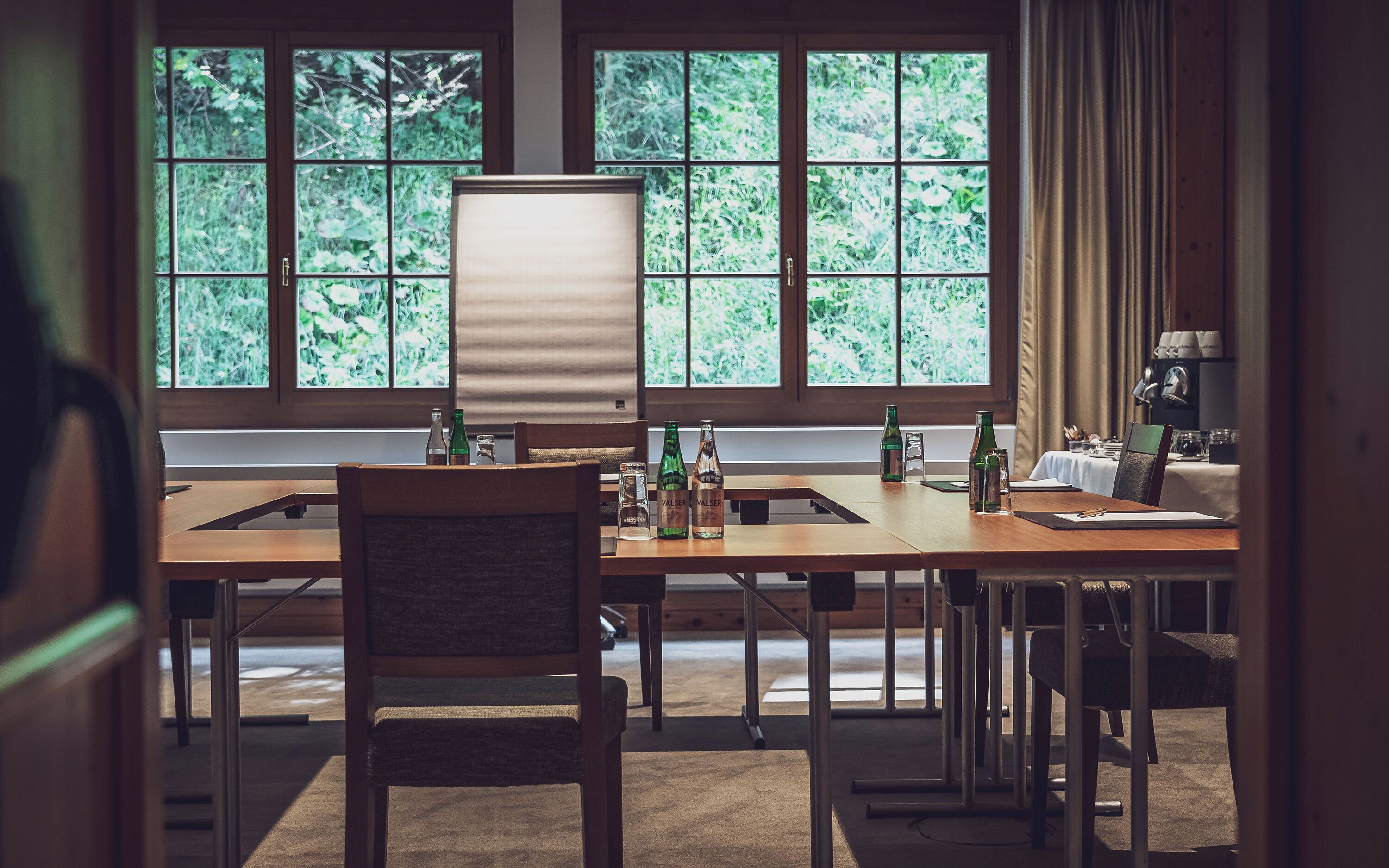 Un salón de conferencias con una mesa grande, sillas y vistas a zonas verdes por las ventanas.