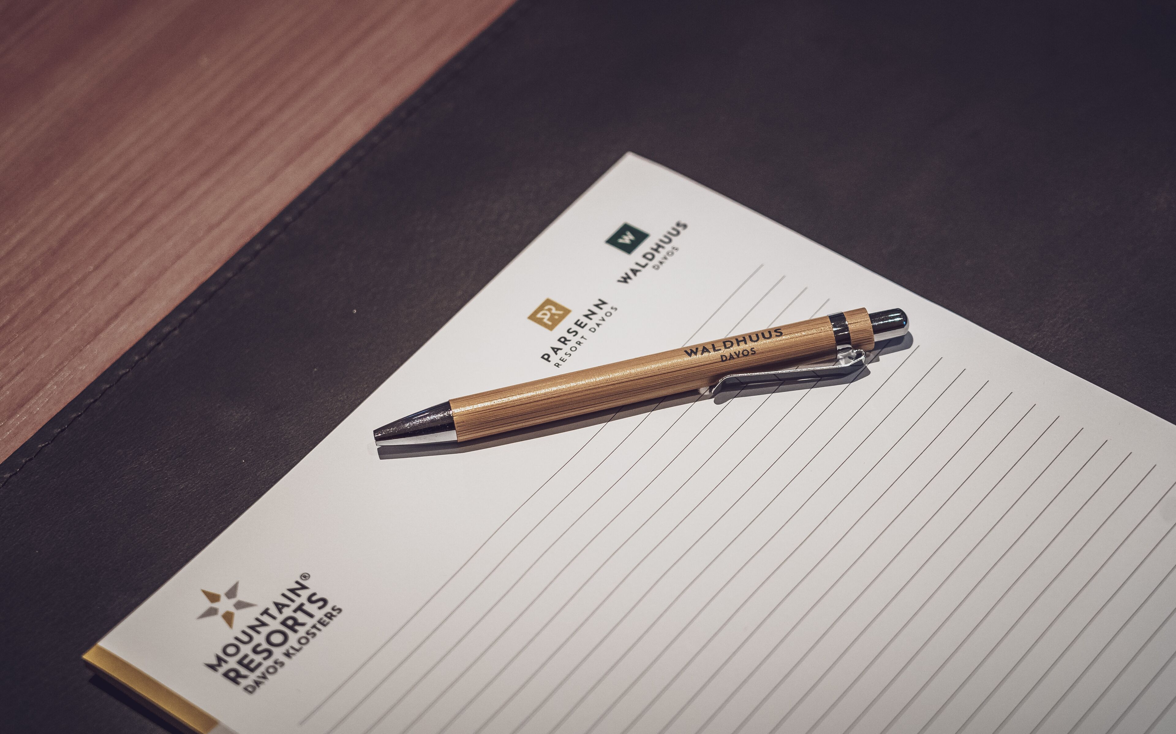Ein Notizbuch mit einem Stift darauf, mit dem Logo von Mountain Resorts und dem Namen 'Waldhuis'.