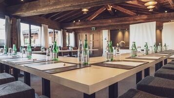 Una larga mesa con varias botellas y copas, ubicada en una habitación con vigas de madera y ventanas amplias.