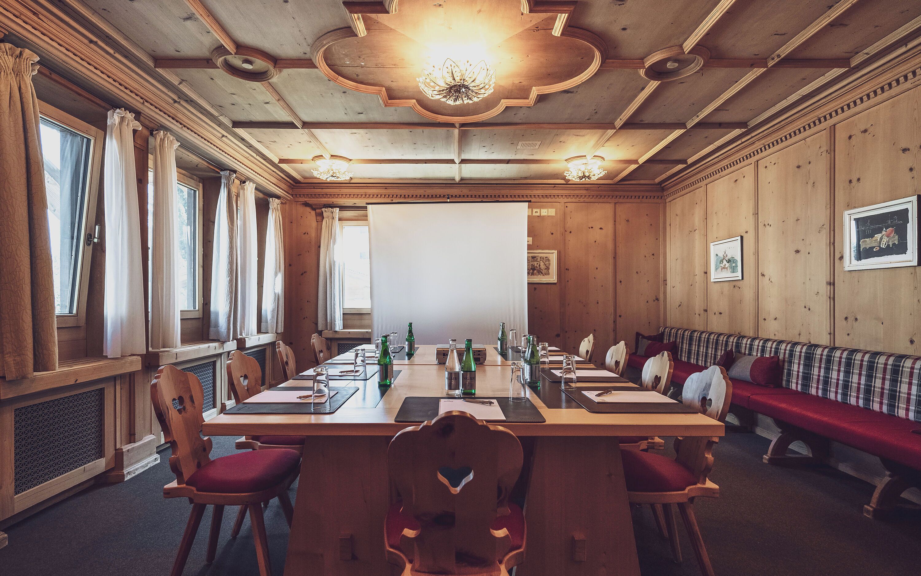 A conference room with a long table, chairs, a bench, wooden walls, and a chandelier.